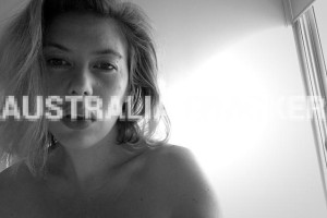 Black and white photograph of a woman with a contemplative expression, half-lit by natural light, with the words 'AUSTRALIA CRACKER' watermarked across the image.