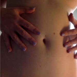 Close-up of two hands with light-purple nail polish gently touching a human belly.
