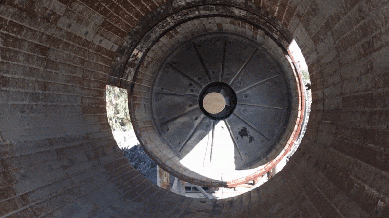 This image presents a unique perspective looking down through a large cylindrical structure with a spiral pattern, focusing on a circular opening at the bottom. 