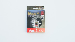 A packaged SanDisk Extreme PRO SDXC UHS-I memory card is displayed on a white gallery wall, and appears to be altered using white out and red texter.