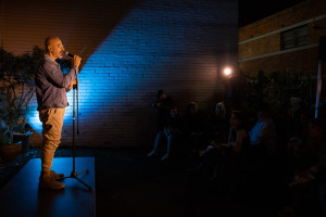 A speaker with a microphone addresses an audience outdoors at night.