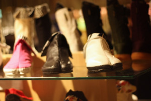 A softly lit display of various shoes, including a pair of bright pink, black, and white footwear on a glass shelf.