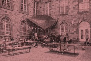 A courtyard in a large stone building with a makeshift kitchen in the corner. People are preparing food.